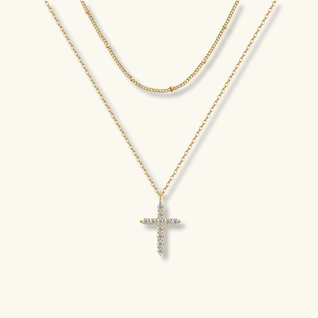 Gold cross necklace with clear stones on a white background
