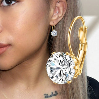 Gold earrings with large clear gemstones worn by a person.
