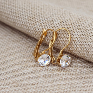Gold earrings with clear gemstones on a beige fabric background