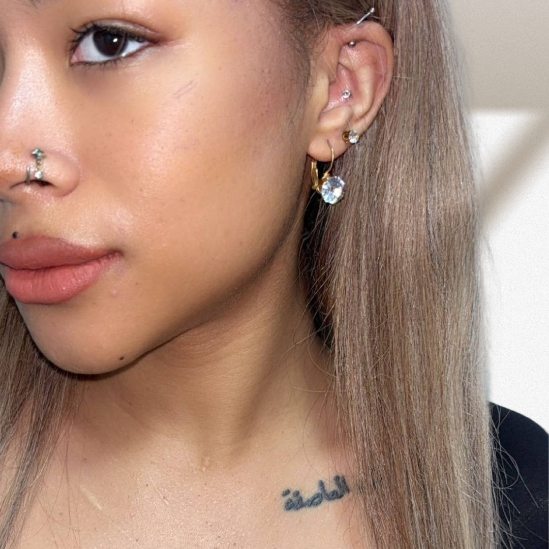 Close-up of a person wearing multiple earrings with a neutral background