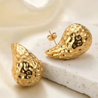 Gold earrings with textured design on a light background