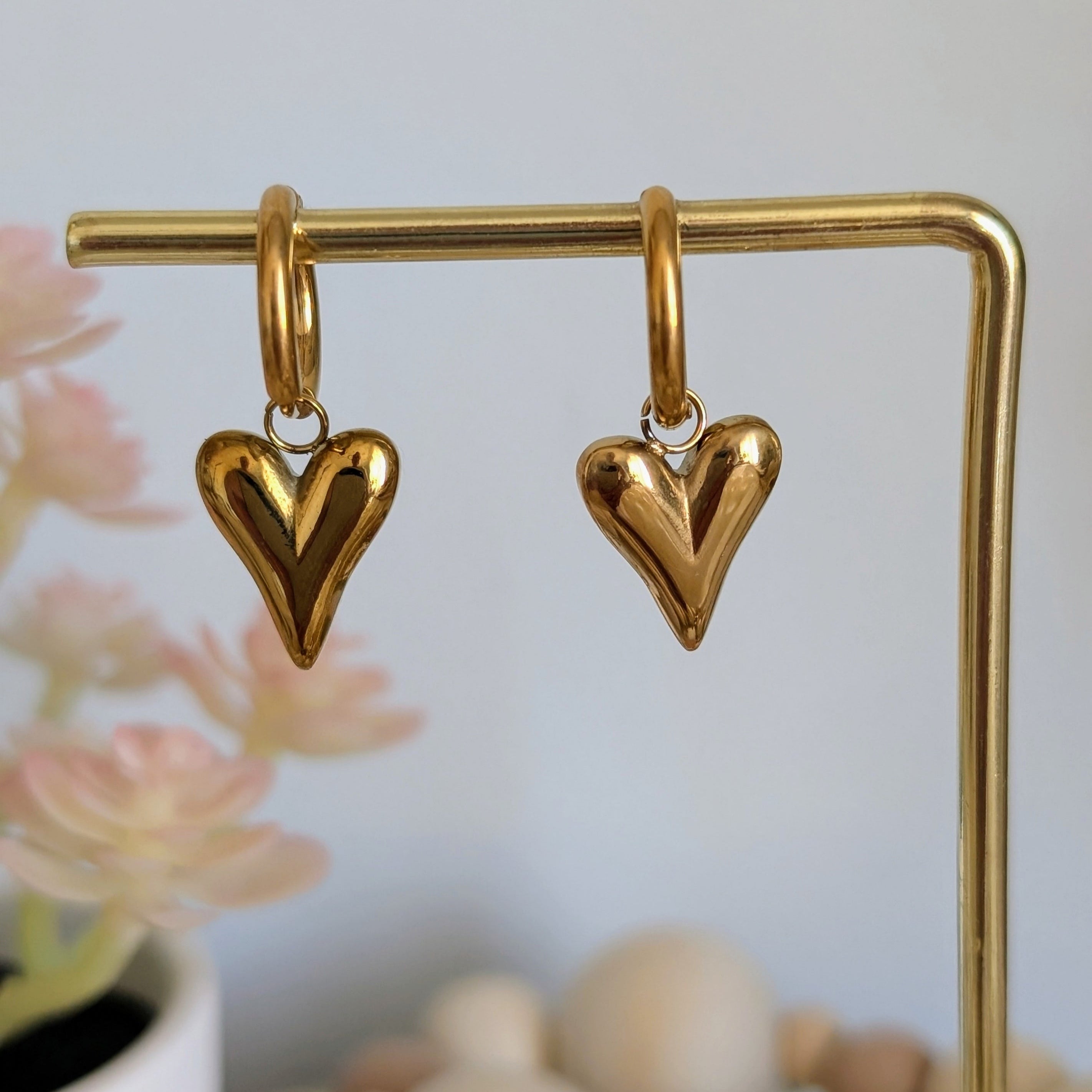 Gold heart-shaped earrings on a gold stand with a blurred background