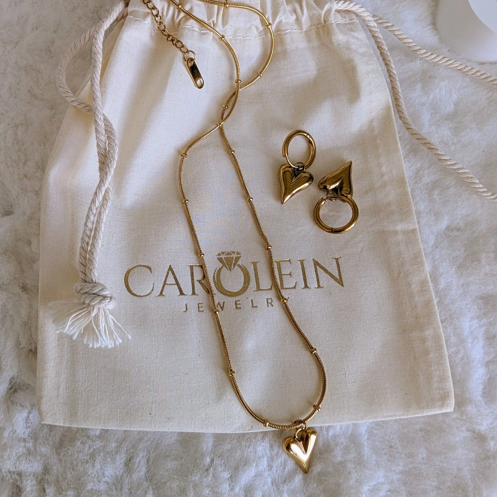 Gold necklace with heart pendants on a Carolinein Jewelry branded drawstring bag.