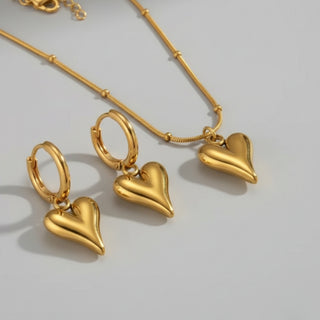 Gold heart-shaped jewelry set including earrings and a necklace on a light gray background