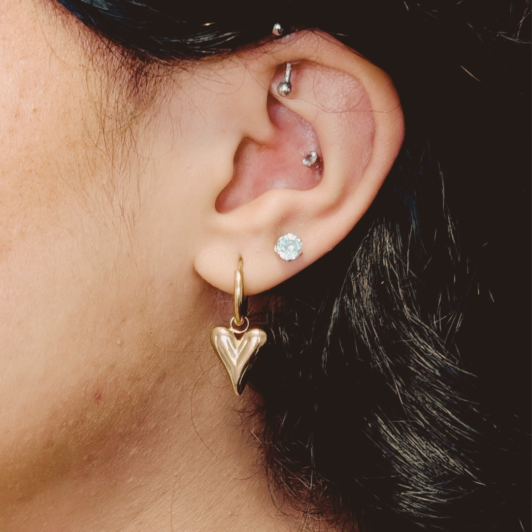 Close-up of an ear with gold heart-shaped earring and silver stud earrings.