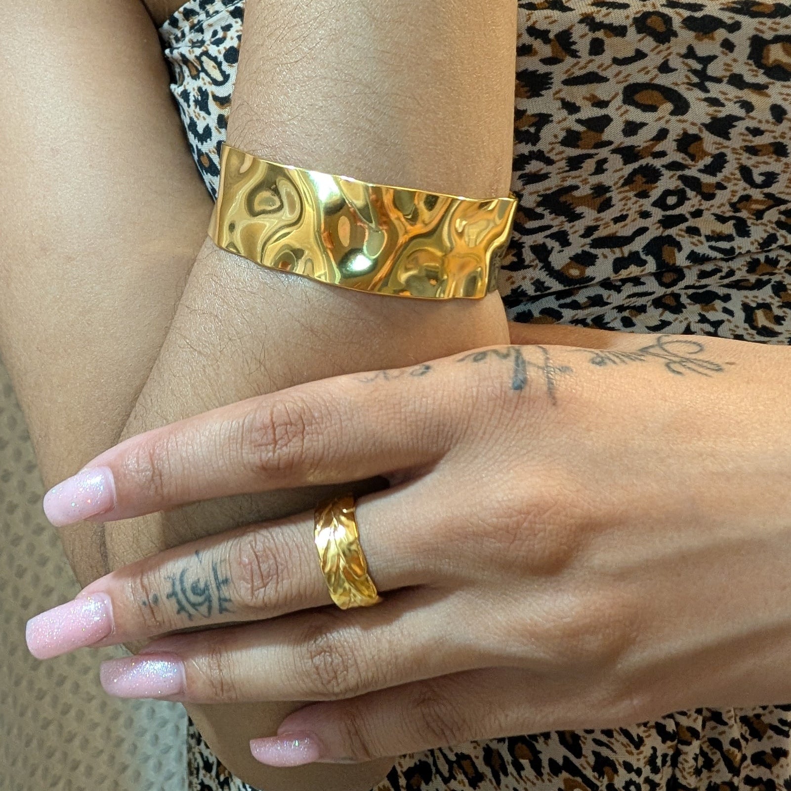 Gold bracelet and ring on a wrist with leopard print fabric in the background
