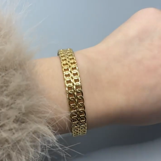 Gold chain bracelet on a wrist with a light blue background
