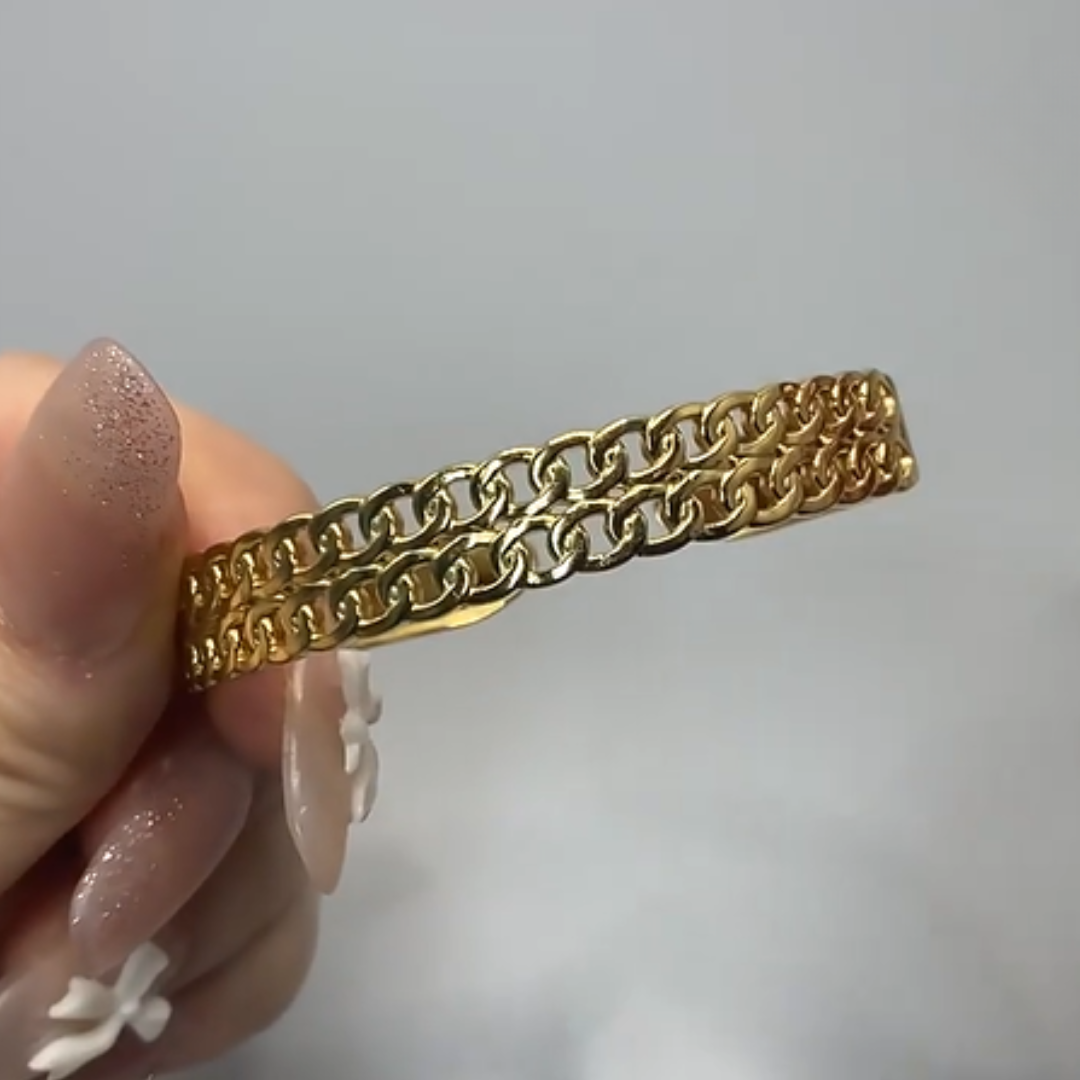 Gold chain bracelet held by a hand with pink nail polish on a light gray background