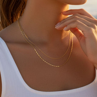 Woman wearing a gold necklace with a blurred beach background