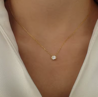 Gold necklace with a small gemstone on a person wearing a beige top.