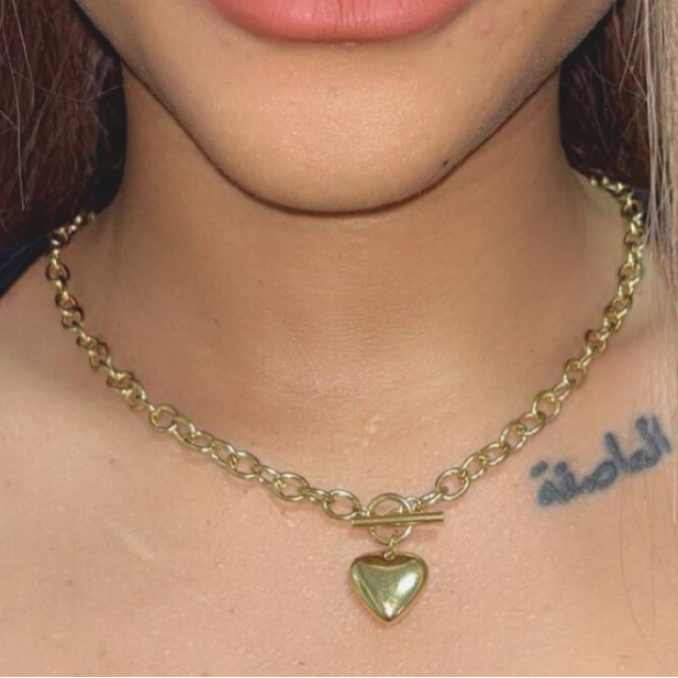 Close-up of a person with a gold chain necklace and heart pendant.