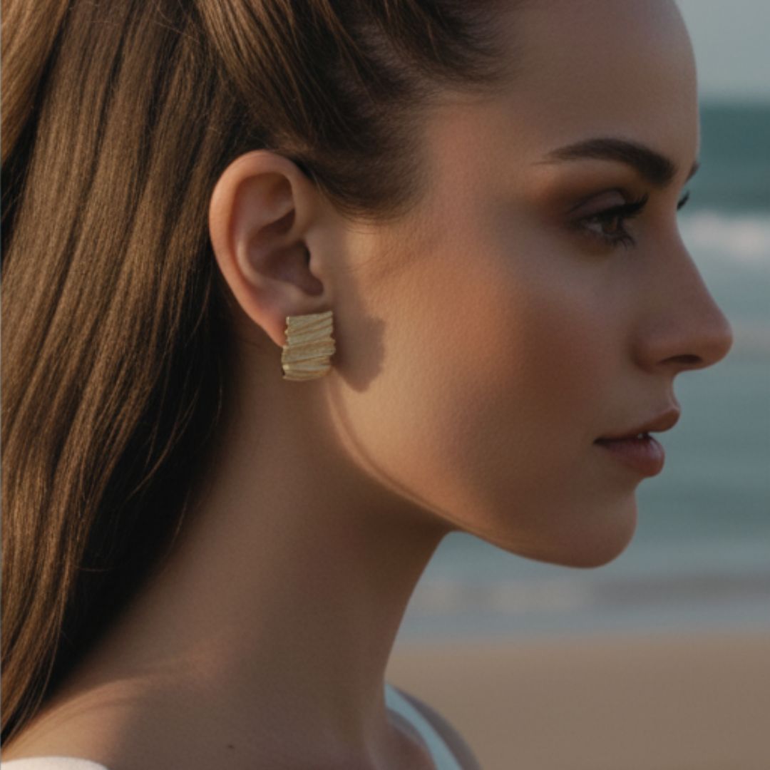Close-up of a woman wearing gold hoop earrings with a blurred beach background