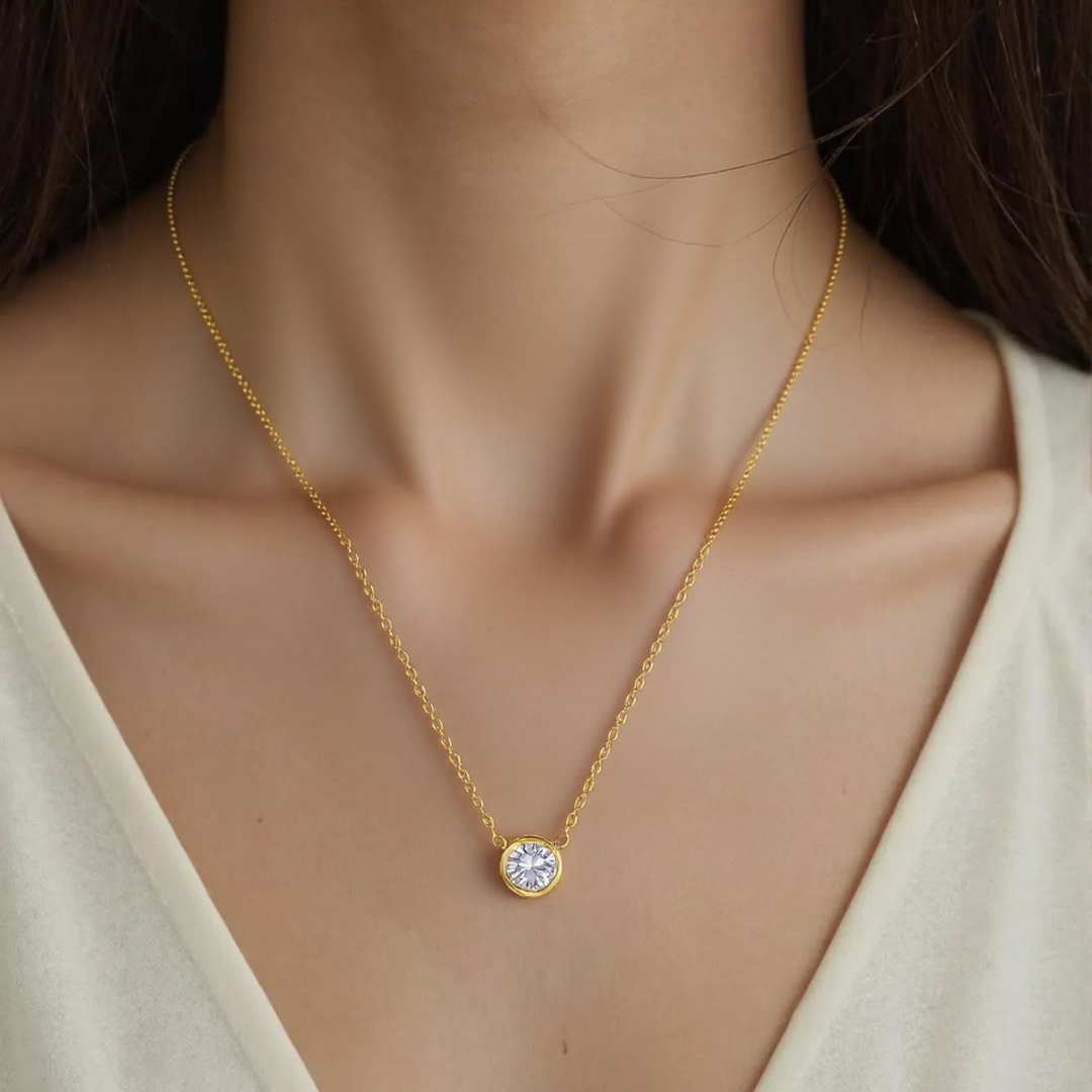 Gold necklace with a small round pendant on a person wearing a beige top.