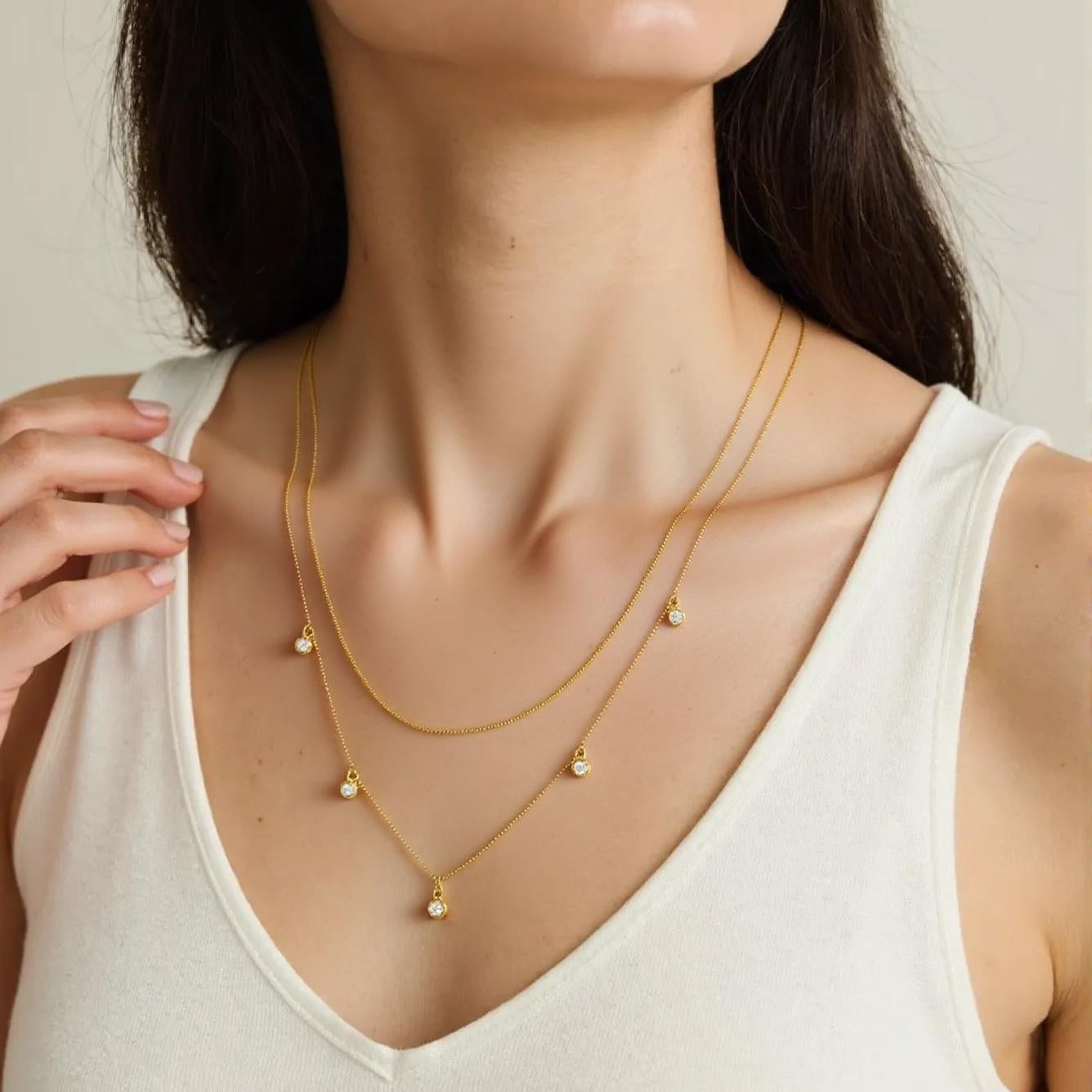 Woman wearing a gold necklace with small pendants on a neutral background