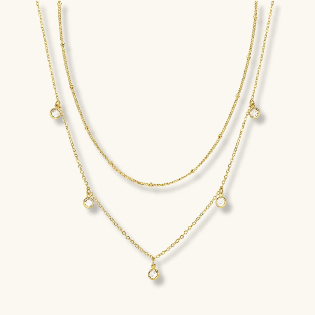 Two gold necklaces with small pendant drops on a white background