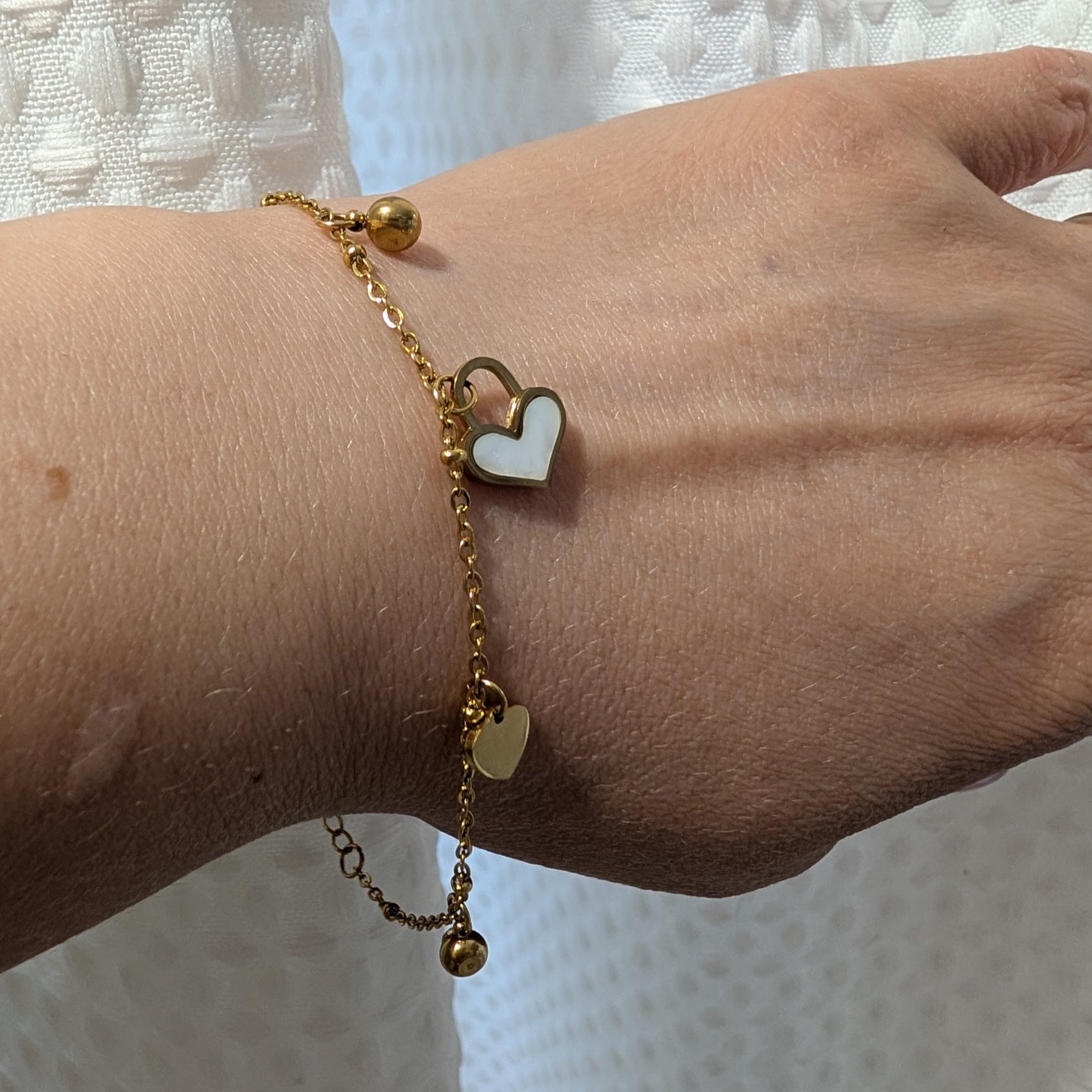 Gold bracelet with heart charm on a wrist against a white textured background