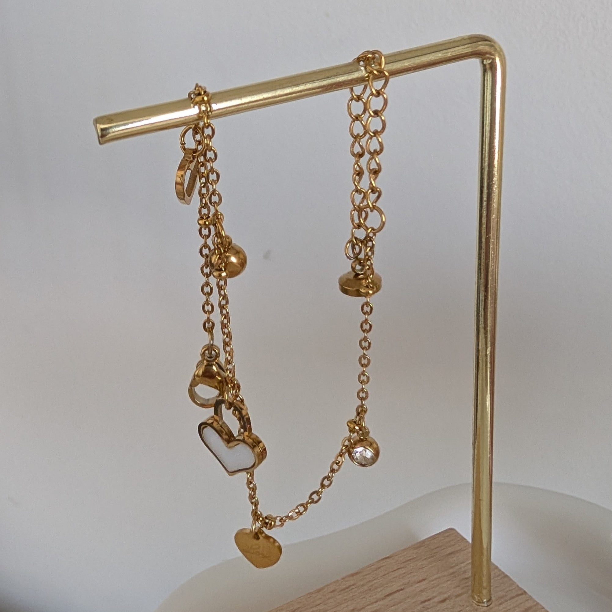 Gold chain bracelet on a gold stand against a white background