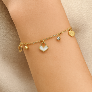 Gold bracelet with heart-shaped charms on a wrist against a beige background