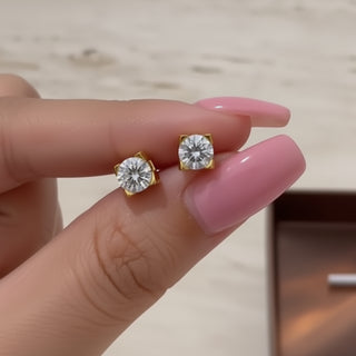 Gold diamond earrings held between fingers with a blurred background