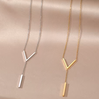 Two necklaces a gold and silver with geometric pendants on a beige fabric background
