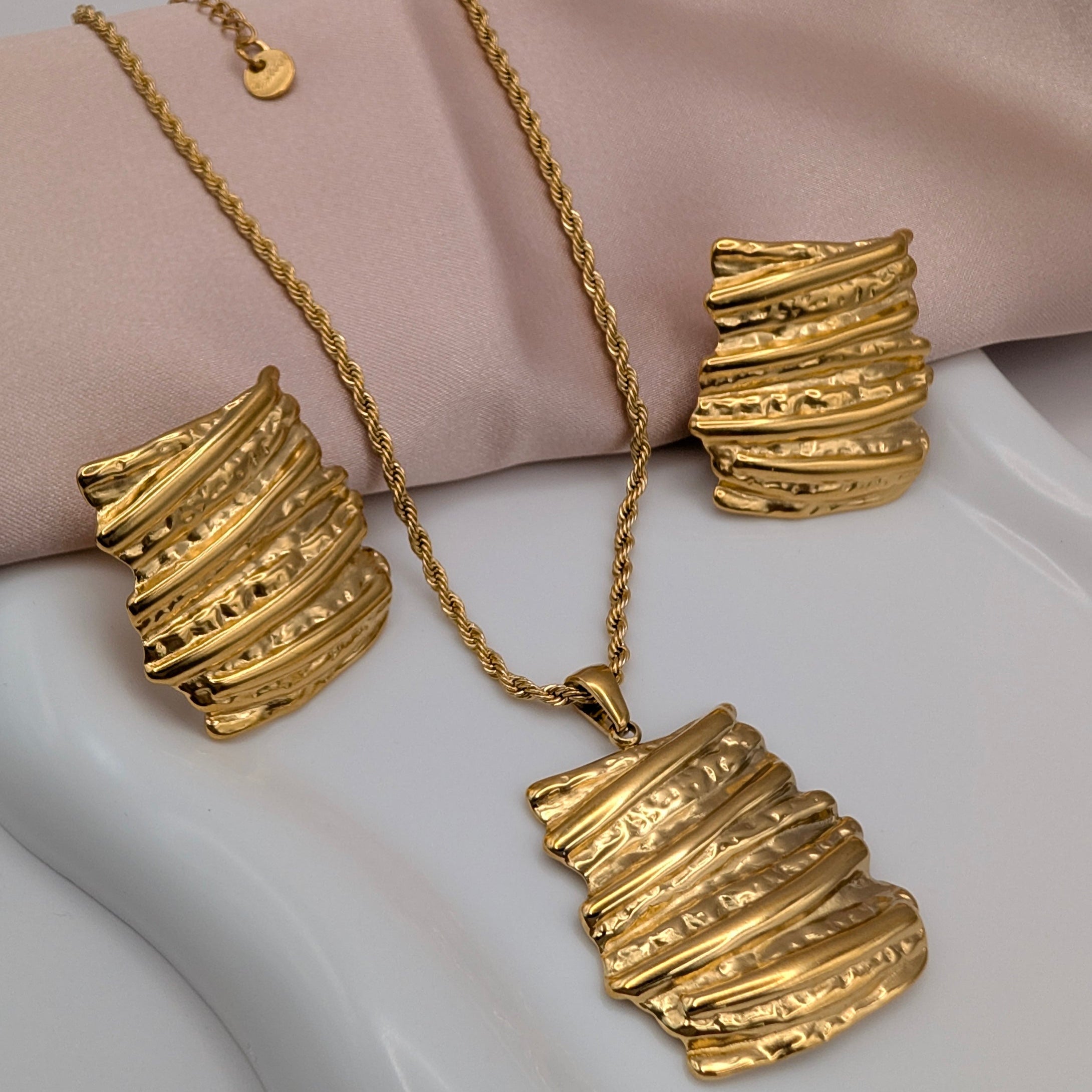 Gold jewelry set including necklace, bracelet, and earrings on a white surface.