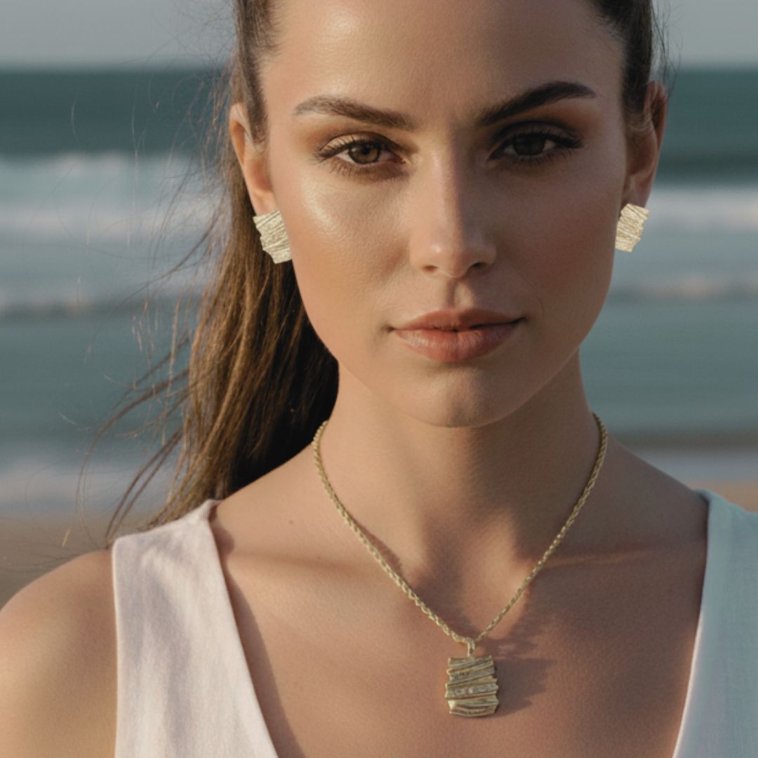 Woman wearing a gold necklace and earrings with a beach background