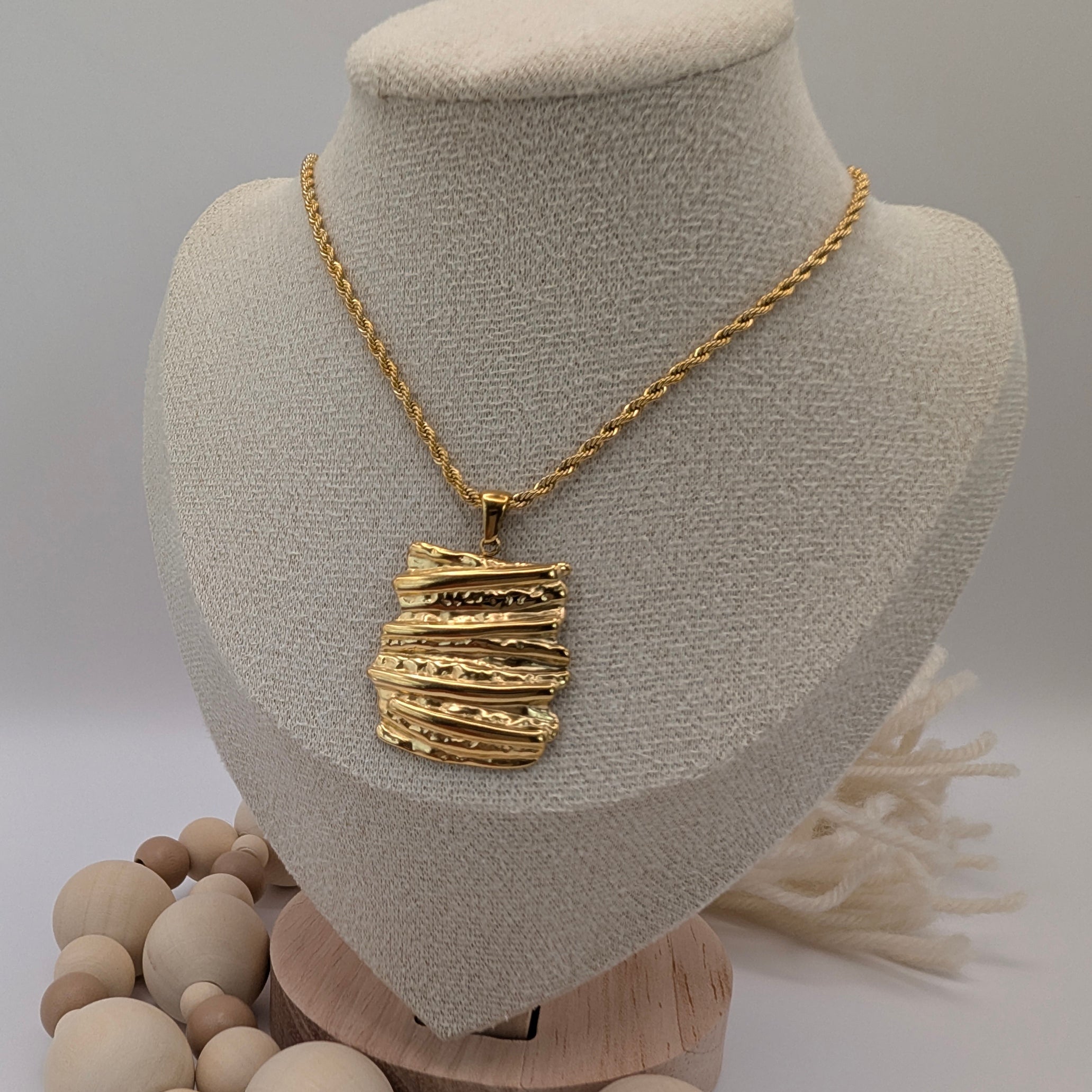Gold necklace with a textured pendant on a mannequin bust, surrounded by wooden beads.