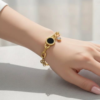 Gold bracelet with a black charm on a wrist against a neutral background