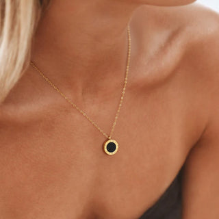 Gold necklace with a black pendant on a person's neck