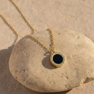 Gold necklace with a black pendant on a stone surface