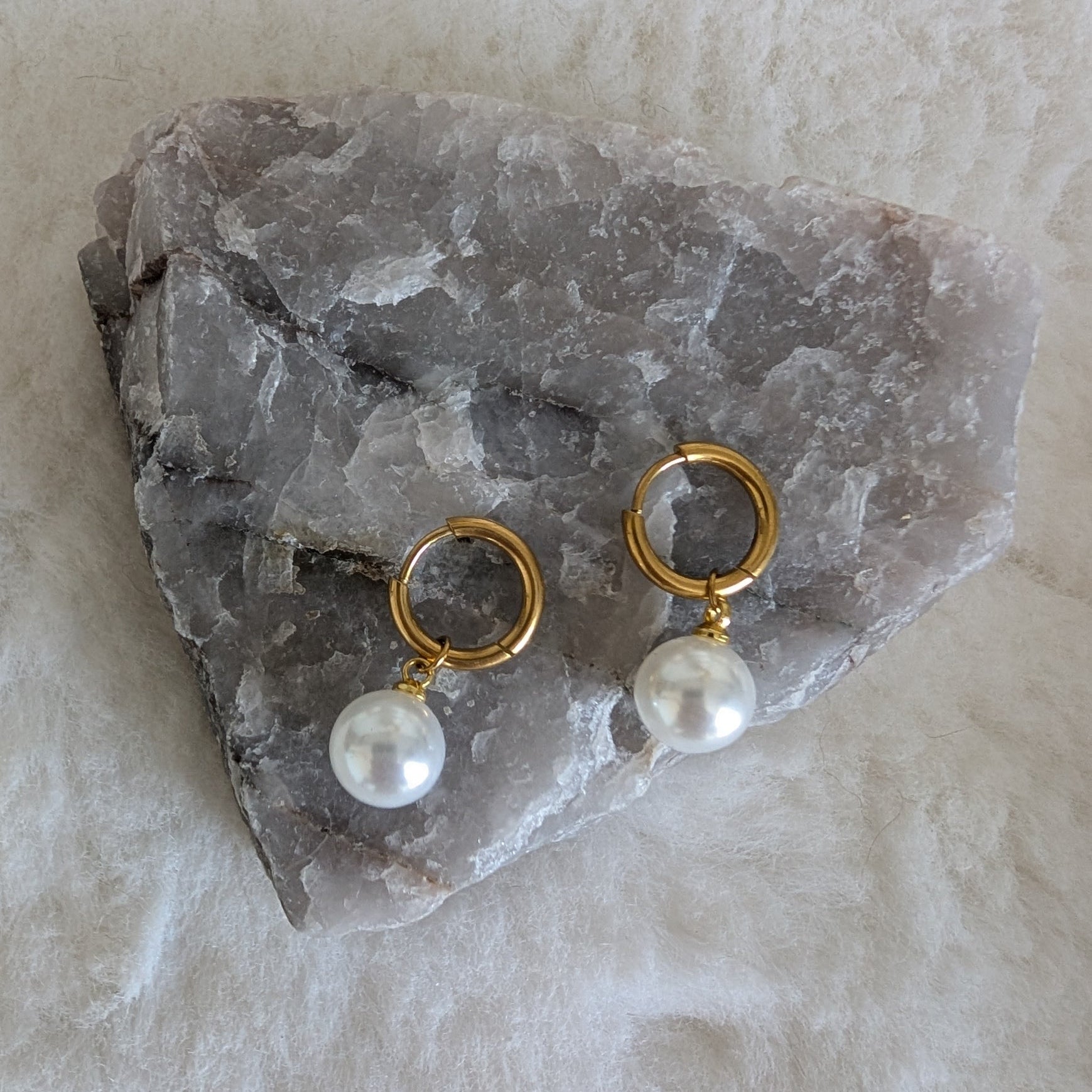 Gold earrings with pearl drops on a stone surface
