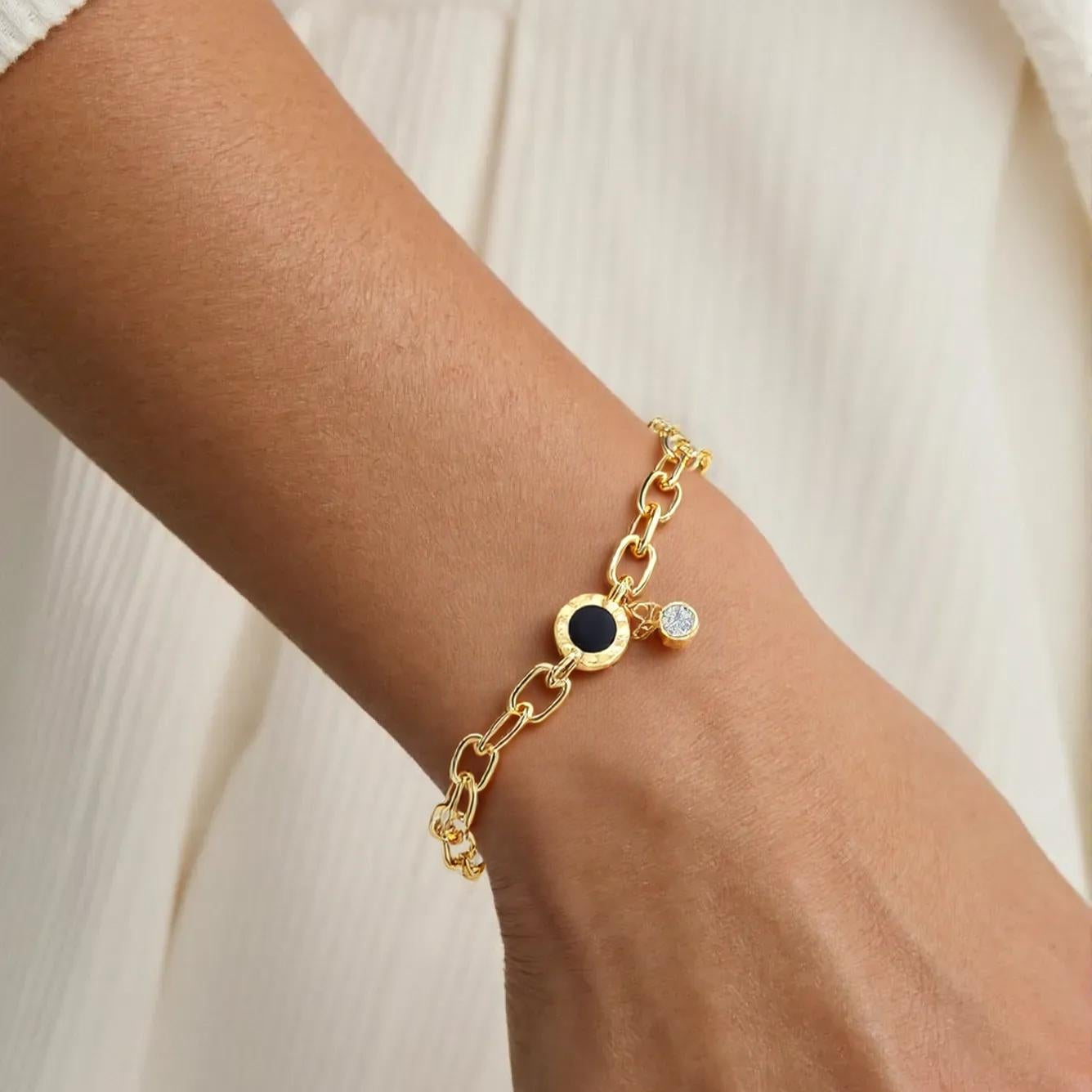 Gold bracelet with gemstones on a wrist against a neutral background