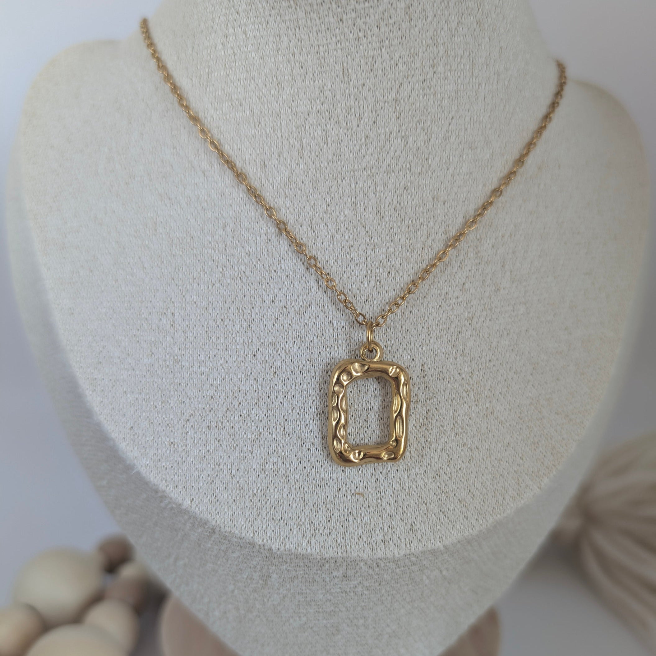 Gold necklace with a textured pendant on a mannequin bust against a white background