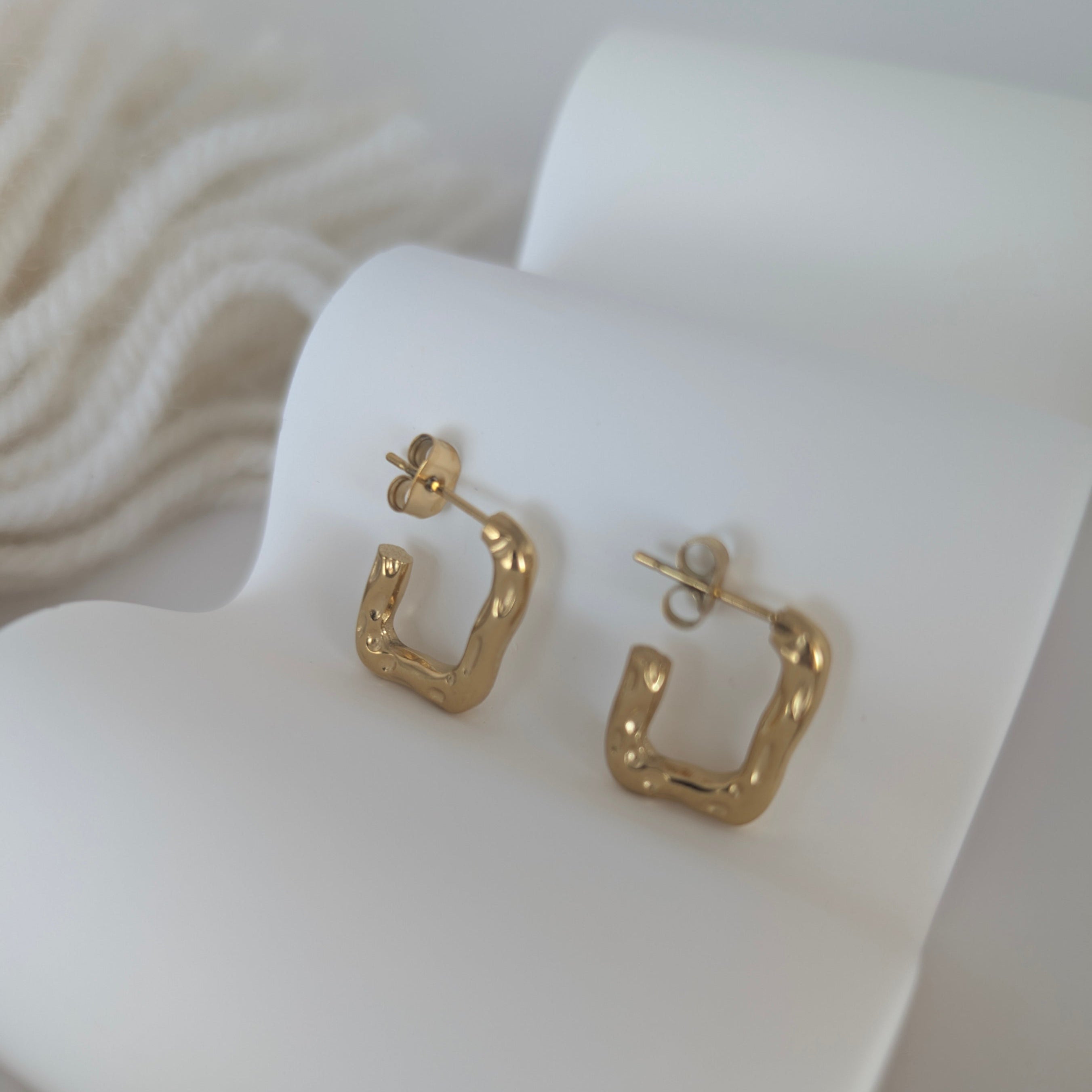 Gold hoop earrings on a white heart-shaped stand
