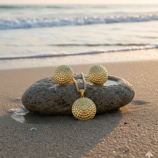Gold textured necklace and earrings on a stone with ocean waves in the background