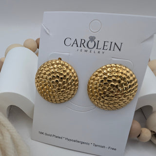 Gold earrings on a Carolein Jewelry card with seashells in the background