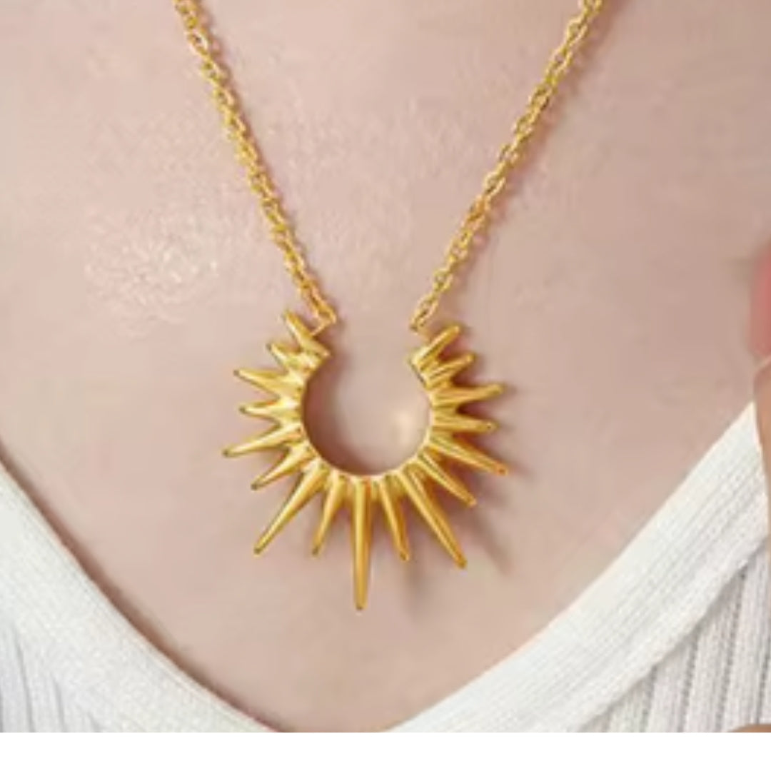 Gold sun-shaped necklace on a person wearing a white top
