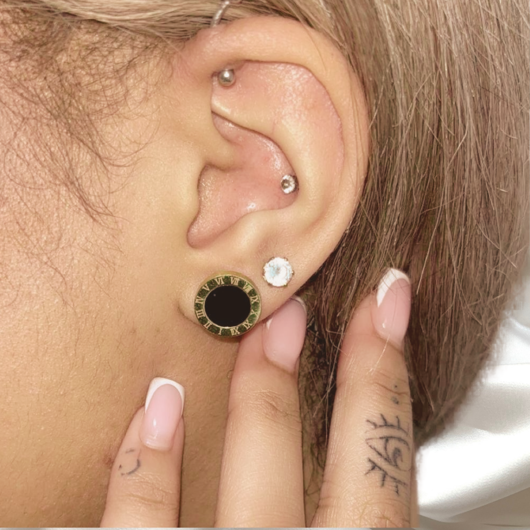 Close-up of an ear with two earrings, one black and gold and one clear, with a hand holding the ear.