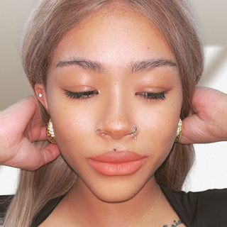 Close-up of a person with a nose ring and earrings, with hands adjusting hair.