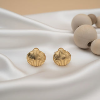 Gold shell-shaped earrings on a white fabric background