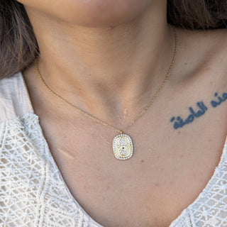 Gold necklace with a evil eye pendant worn by a person with a tattoo on their chect