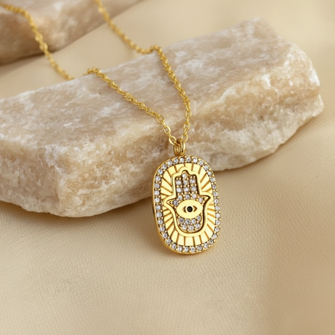 Gold necklace with a Hamsa hand pendant on a beige stone surface