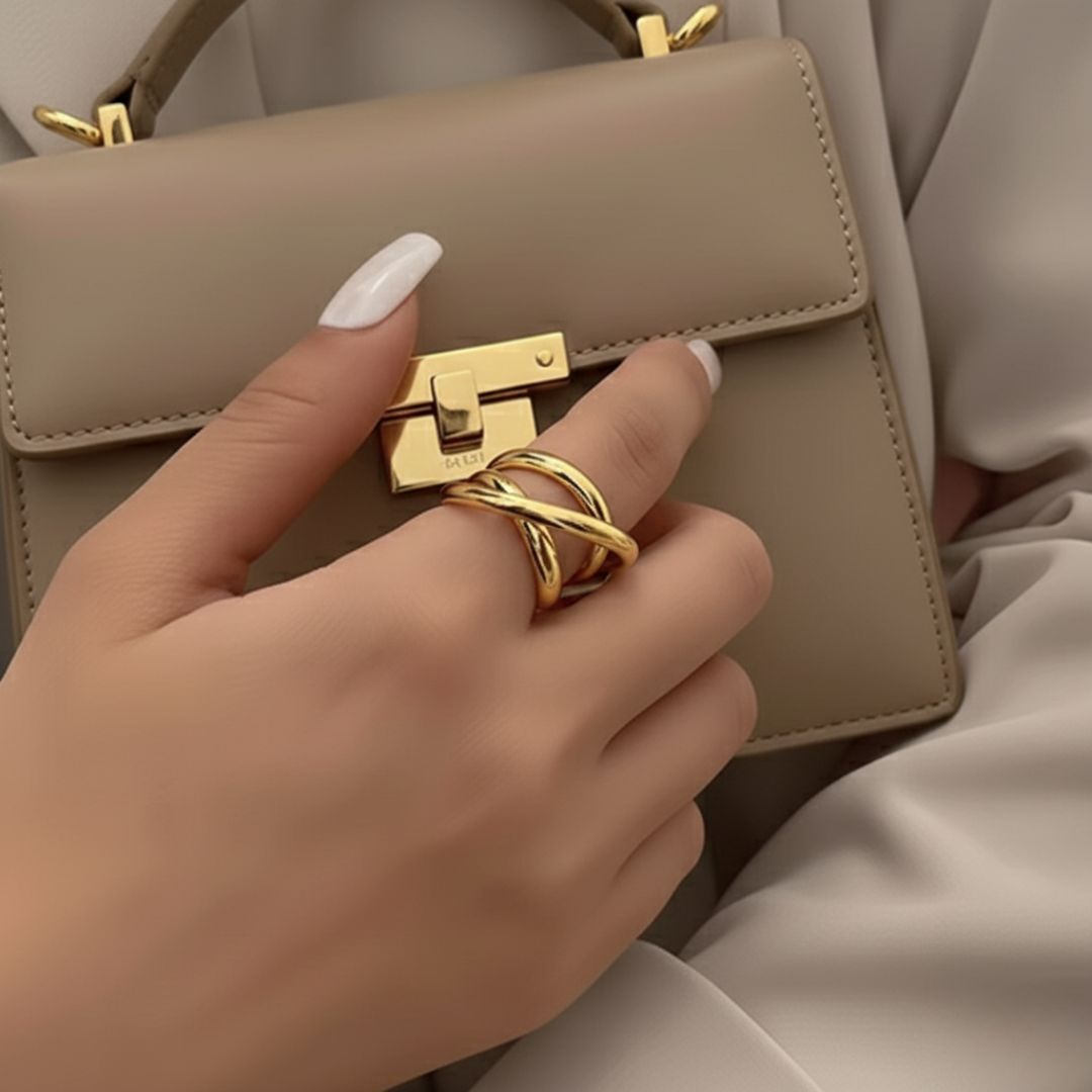 Hand holding a beige handbag with a gold lock and matching ring.