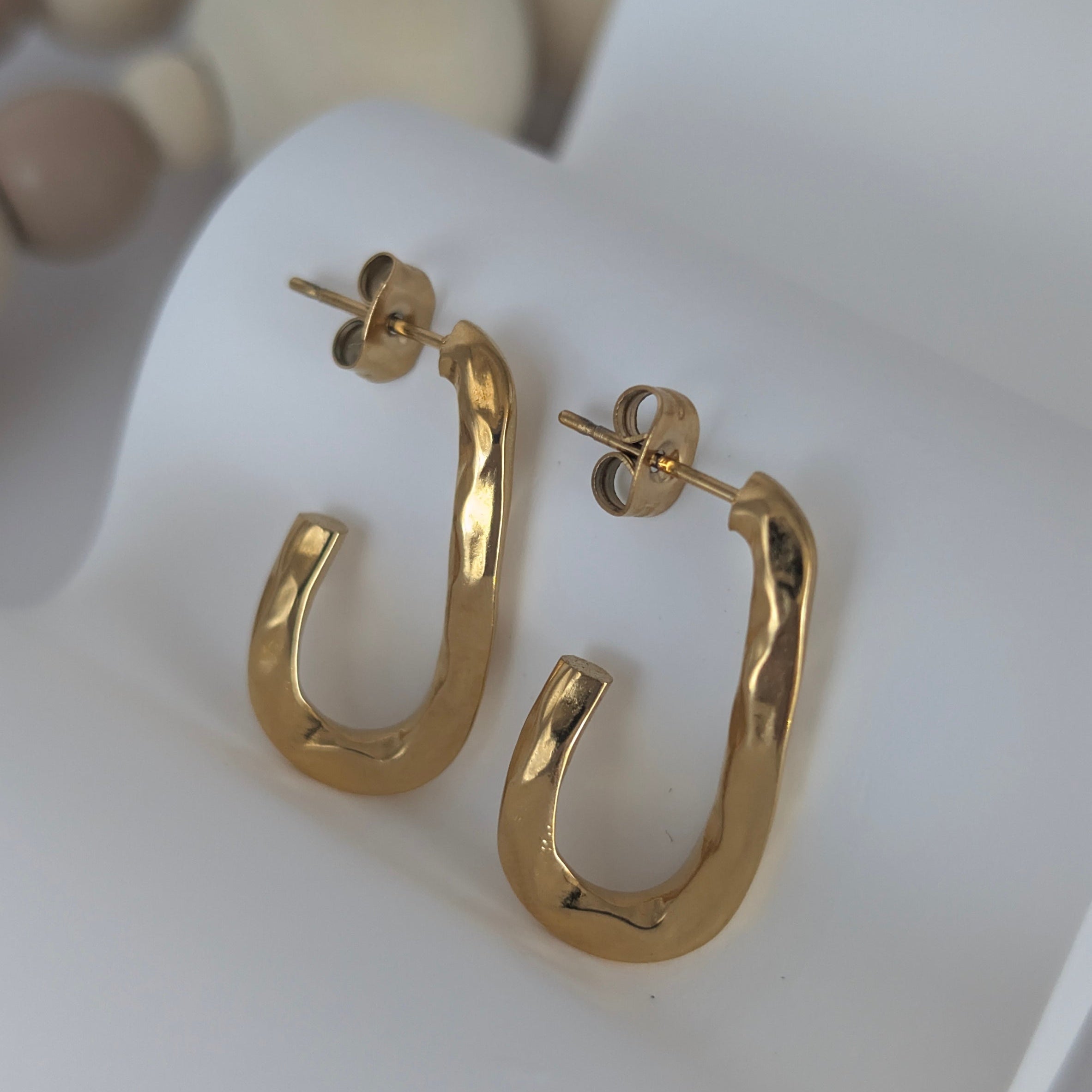 Gold hoop earrings on a white surface with a blurred background