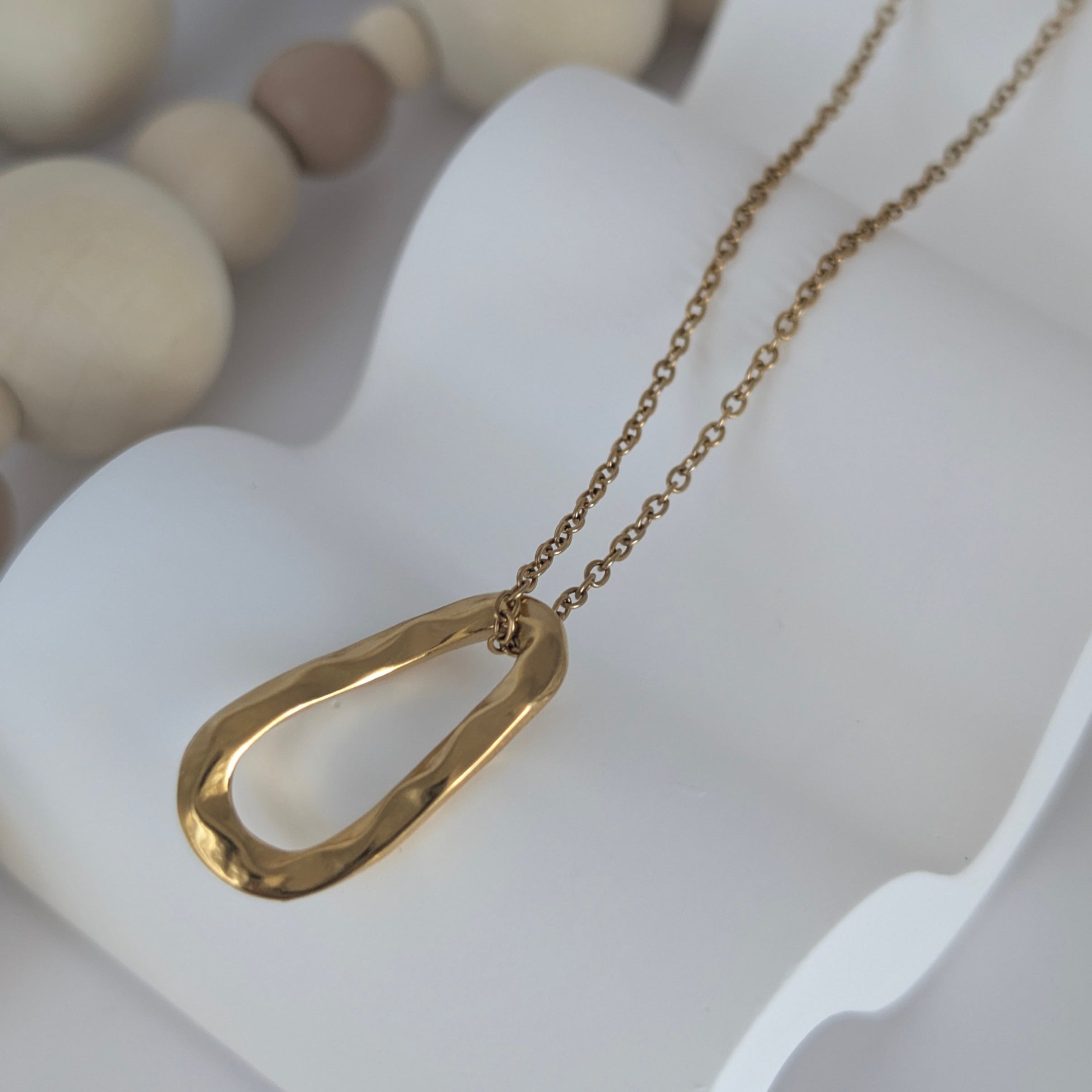 Gold necklace with a unique pendant on a white stand with wooden beads in the background