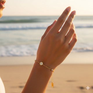 Hand wearing a gold bracelet on a beach with ocean in the background