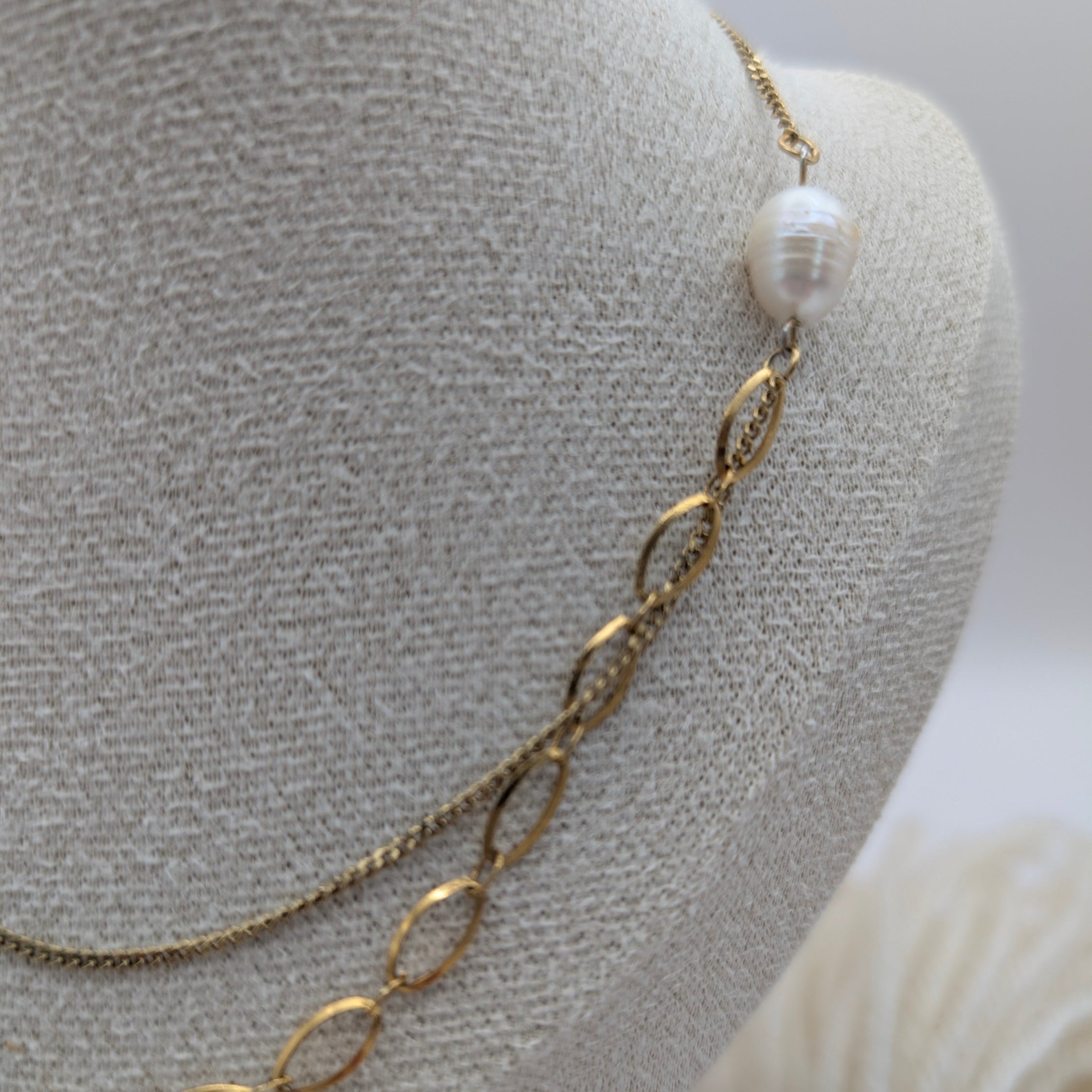 Gold chain necklace with a pearl on a mannequin bust.