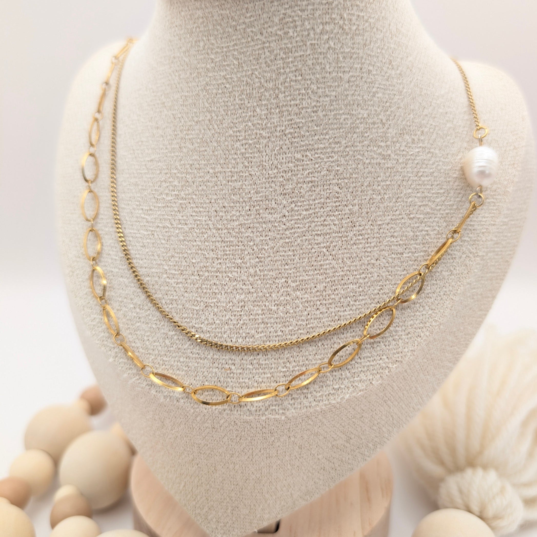 Gold chain necklace on a mannequin bust with wooden beads in the foreground