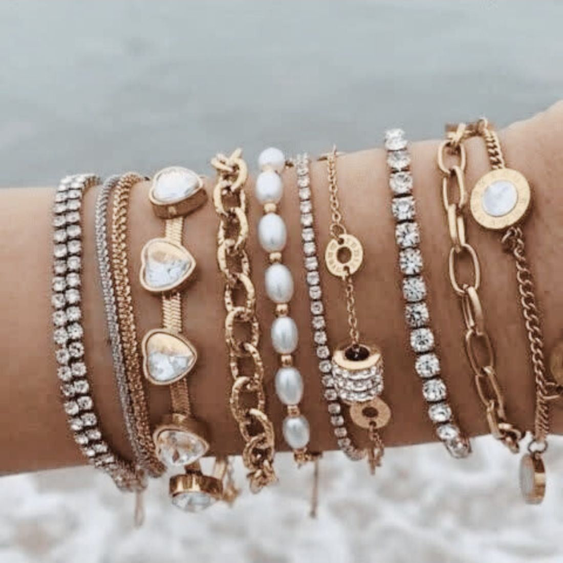Multiple gold and pearl bracelets on a wrist against a light background