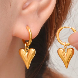 Gold heart-shaped earrings being worn on an ear with a blurred background